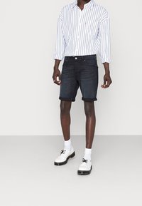 Blå denimshorts med uppvikta nederkanter, kombinerat med en vit och blå randig långärmad skjorta och vita snörskor.