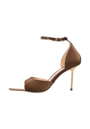 Smeđa satenska sandala na štiklu s otvorenim prstima, tankim zlatnim remenom oko gležnja s malim šiljcima i zlatnom visokom petom s crnim vrhom.