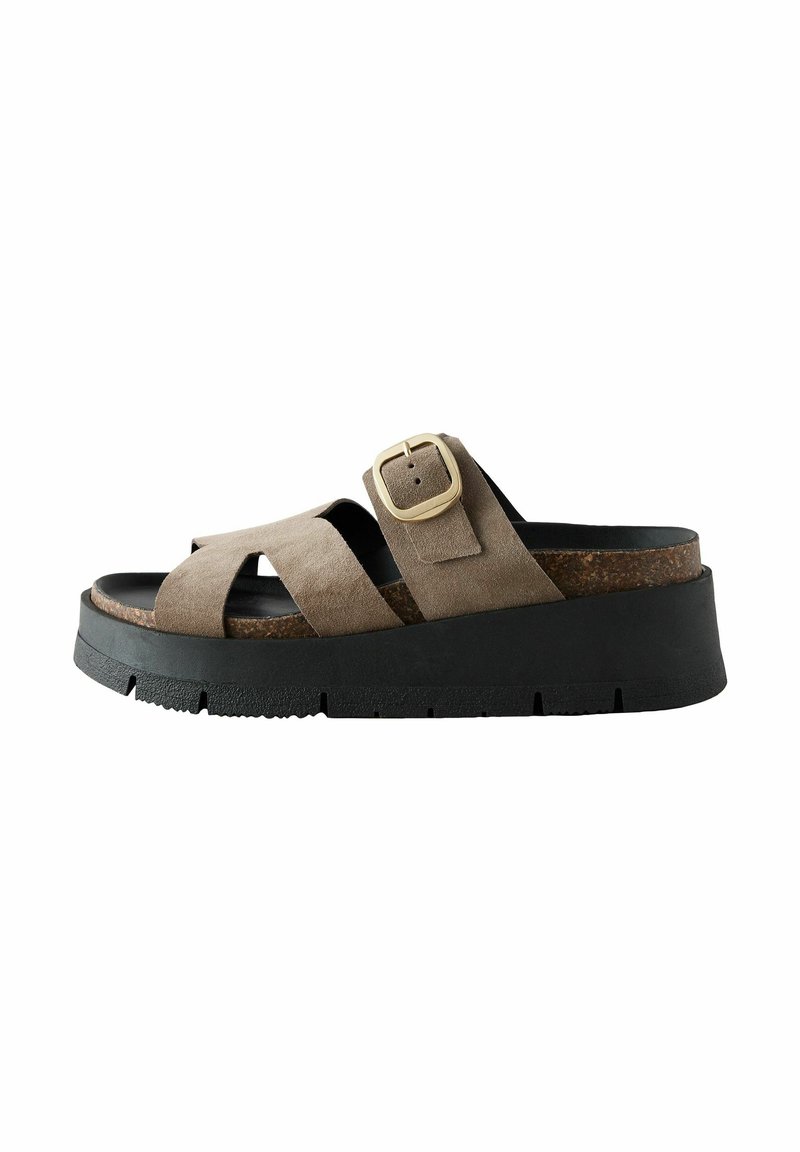 Suedestrop sandal i tan med en bred krydset overrem, guldspænde detaljer og en kraftig sort gummisål med struktur.