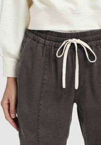 Close-up van een persoon die donkere grijze drawstring broek draagt met een witte touw in een strik en een deel van een witte sweatshirtmouw is gedeeltelijk zichtbaar.