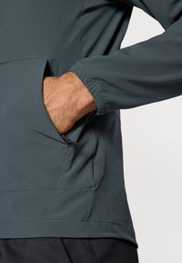 Mørkegrå pulloverjakke med en lynlåslomme og elastiske manchetter; glat tekstur; designet til komfort og funktionalitet.