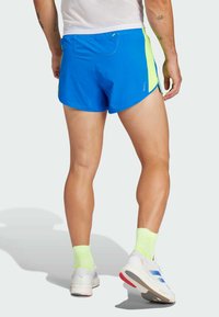 Blauwe sportshorts met groene accenten, ademend materiaal en een achterzak. Draagt met witte schoenen en lichtgroene sokken.