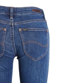 Jeans de mezclilla azul oscuro con un diseño ajustado, que presentan bolsillos traseros con costuras curvadas y un pequeño logo de Lee en un bolsillo.