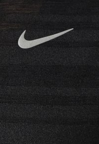 Tejido atlético negro con un patrón texturizado y sutiles rayas. Un logotipo plateado de Nike está exhibido de manera prominente.