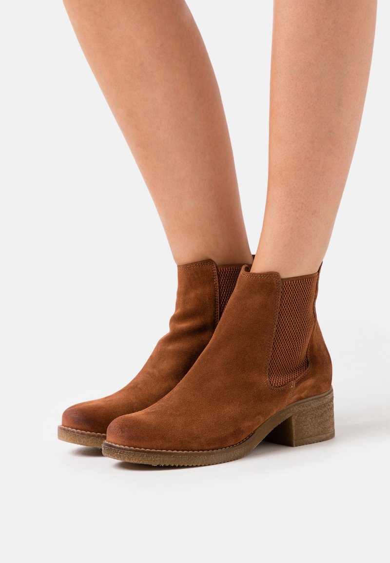 Brown suede ankle boots with elastic side panels and a textured block heel. Smooth surface with rounded toe, designed for easy wear.