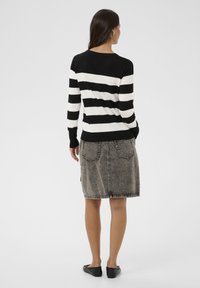 Pull rayé noir et blanc à manches longues, assorti à une jupe en denim gris avec poches et ourlet brut, porté avec des ballerines noires.