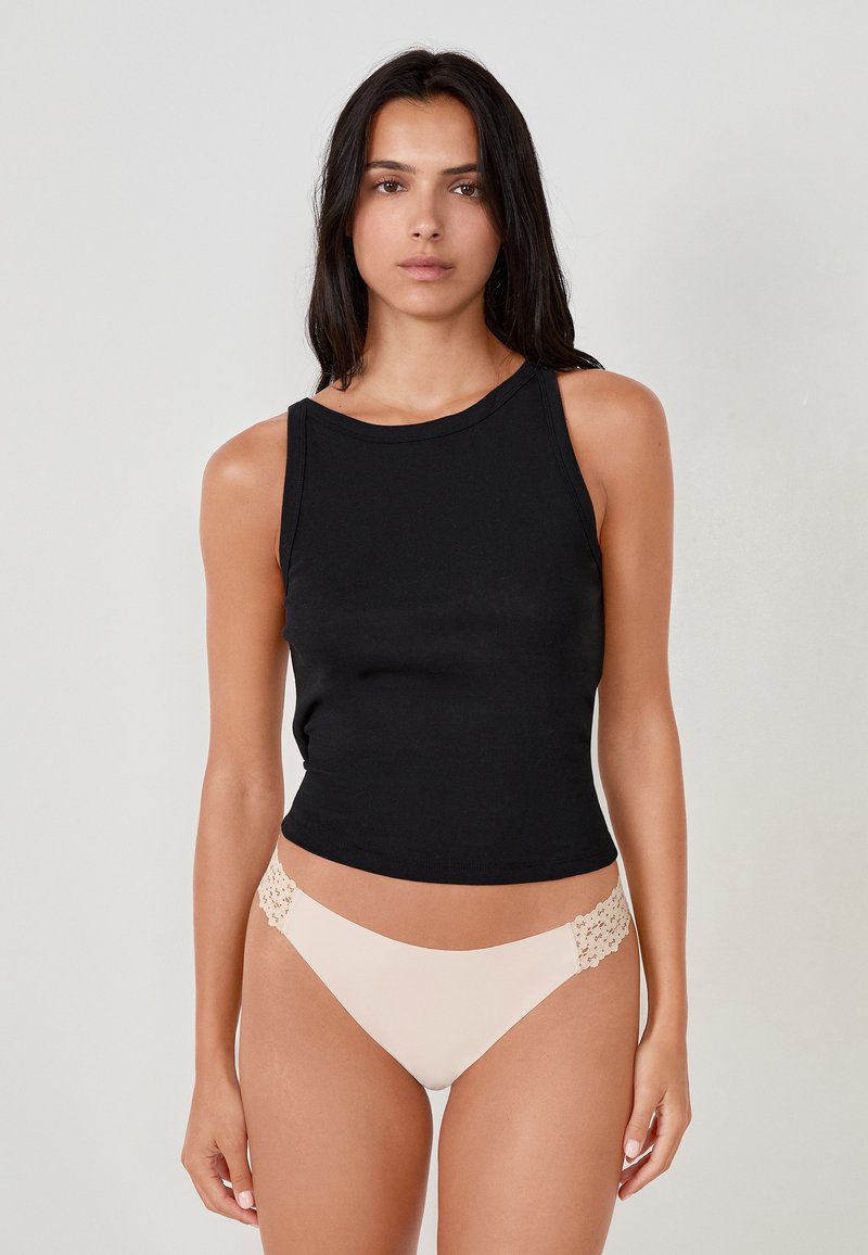 Top in cotone nero aderente con scollo tondo, abbinato a slip da bikini beige con dettagli in pizzo sui fianchi. Texture liscia, design minimale.