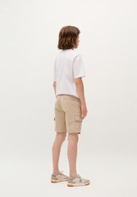 Camicia bianca a maniche corte, pantaloni cargo color khaki con tasche laterali e scarpe beige con accenti blu, viste da dietro. Design semplice.