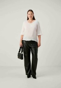 Balta, lengva bliuska trumpomis rankovėmis, suderinta su juodomis aukštu liemeniu odinėmis kelnėmis. Modelis laiko mažą juodą rankinę.