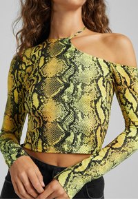 Långärmad crop top i ormskinnsmönster; gula och svarta färger; textural mönster; har en skärning på axlarna.