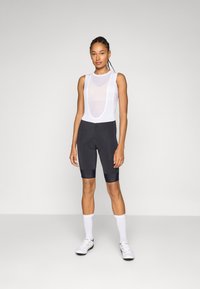 Damen-Radsportoutfit mit einem weißen Mesh-Tanktop und schwarzen Shorts, entworfen für Komfort mit gepolstertem Sitz. Strukturierter, körperbetonter Stoff.