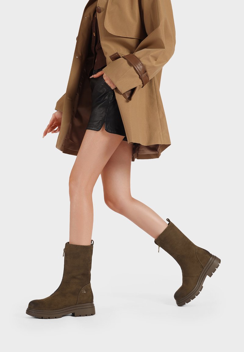 Stivali alla caviglia in suede marrone con punta tonda e suola spessa. Dettaglio con zip sul lato e linguetta sul retro per una facile indossabilità.