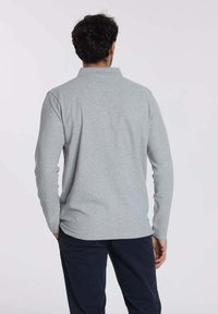 Polo à manches longues gris clair en tissu doux, doté d'un col et d'un ourlet droit. Stylé avec des coutures minimales et sans logos visibles.