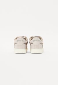 Reebok sneakers with a beige suede upper, perforated detailing, and cream rubber soles, featuring a subtle logo on the back.