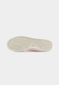 Σόλα άσπρου παπουτσιού Nike με ανάγλυφο σχέδιο ζιγκ-ζαγκ και λογότυπο Nike στο τόξο, εμφανίζεται πάνω σε απλό φόντο.