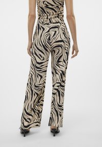 Beige weite Hosen mit einem schwarzen abstrakten Wellenmuster. Hergestellt aus strukturiertem Stoff, mit hoher Taille und seitlichen Schlitzen am Saum.