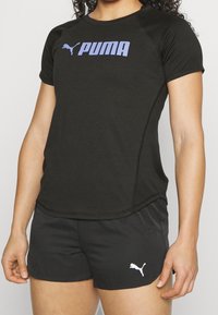 Černé sportovní tričko s fialovým logem "PUMA", doplněné černými šortkami, obě vyrobené z materiálu odvádějícího vlhkost s přiléhavým střihem.