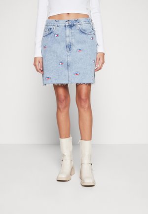 Denim minirok met kleine rode en blauwe lapjes, gecombineerd met witte hoge hak midkuitlaarzen en een wit cropped top met lange mouwen.