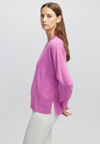Roze, langmouwige trui met een V-hals, met een ontspannen pasvorm en zijsplitten, gecombineerd met witte, strakke broek. Gladde textuur.