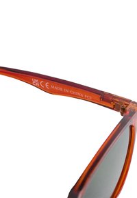 Close-up van een oranjebruine brillenpoot met CE- en UKCA-certificeringsmerken en de tekst "Made in China FC3".