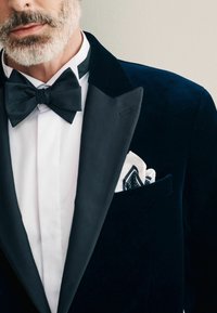Crni baršunasti tuxedo satenastim reverima, bijela košulja i crna leptir mašna. Marama u džepu ukrašena je uzorkom točkica u crnoj i bijeloj boji.