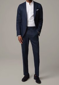 Marinblå linnkostym med skräddarsydd passform, parat med en vit skjorta med krage. Mörka loafers fulländar den smart-casual looken.