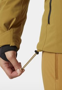 Geel softshelljack met zwart accent, met een hand die een trekkoord aan de manchette aanpast. Glad textuur met draagbaar ontwerp.