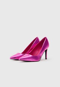 Sæt af skinnende metallisk pink højhælede sko med spidse tæer og sorte stiletter på en neutral baggrund.