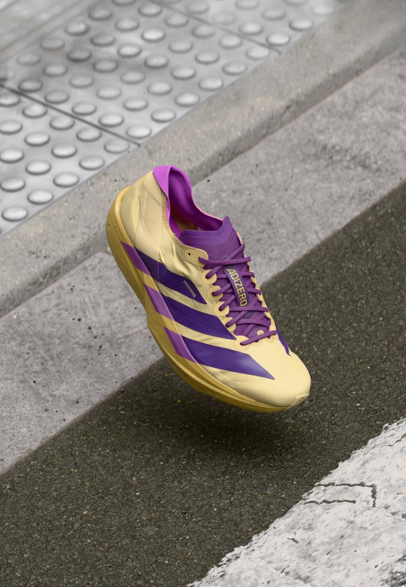 Chaussure de course jaune et violette au design épuré, dotée d'un matériau léger, de lacets violets et de trois bandes latérales violettes.