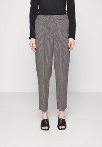 Person wearing high-waisted, tapered checkered pants with pleats, black long-sleeve top, and black open-toe heeled mules.