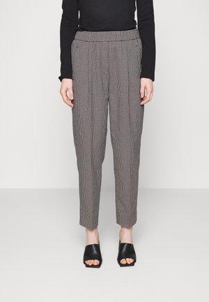 Personne portant un pantalon à carreaux taille haute et fuselé avec des plis, un haut noir à manches longues et des mules à talons ouverts noires.