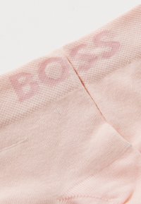 Svetloružové ponožky vyrobené z jemného materiálu, s textúrovaným dizajnom a subtilne integrovaným nápisom "BOSS" na vrchu.