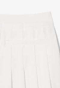 Tela blanca con pliegues que presenta una cinturilla limpia y un bolsillo trasero discreto. Textura suave con pliegues bien definidos.