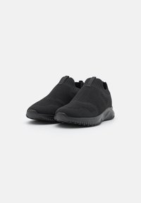 Zwarte instap sport schoenen met een getextureerde gebreide bovenkant, elastische bovenbanden en een flexibele rubberen zool met een golvend ontwerp.
