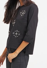 Top de algodón negro con mangas tres cuartos y diseños florales embellecidos con cuentas y lentejuelas en la parte delantera.