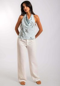 Haut sans manches bleu clair avec un col drapé et des broderies florales argentées, accompagné de pantalon blanc ample et texturé ainsi que de sandales.