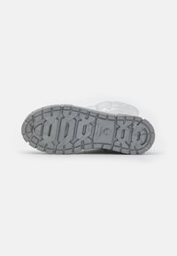 Bota transparente con una suela de goma texturizada en gris. Presenta un diseño de patrón múltiple para agarre y tracción. Material superior suave.