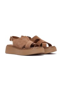Sandali in suede marrone con suola piatta, dotati di cinghie incrociate e fibbia regolabile alla caviglia. Texture liscia con dettagli di cuciture visibili.