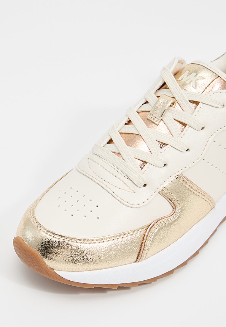 Baskets beiges avec accents métalliques dorés, cuir texturé et languette rembourrée. Comprend une semelle en caoutchouc blanche et des lacets plats.