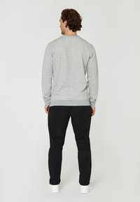 Sudadera gris con puños y dobladillo acanalados, combinada con pantalones negros y zapatillas blancas. La textura parece suave; el diseño es simple y funcional.