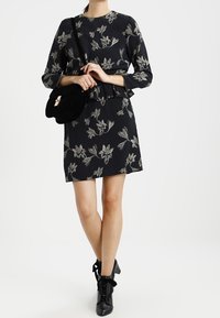 Svart klänning med blommönster, trekvartslånga ärmar och peplummidja. Matchad med en svart crossbody-väska och ankellånga stövlar.