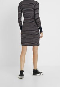 Sweterkowa sukienka o dopasowanej sylwetce, w poziome pasy w kolorze granatowym i kremowym, z długimi rękawami i ściągaczami przy mankietach, zestawiona z czarnymi sneakersami.