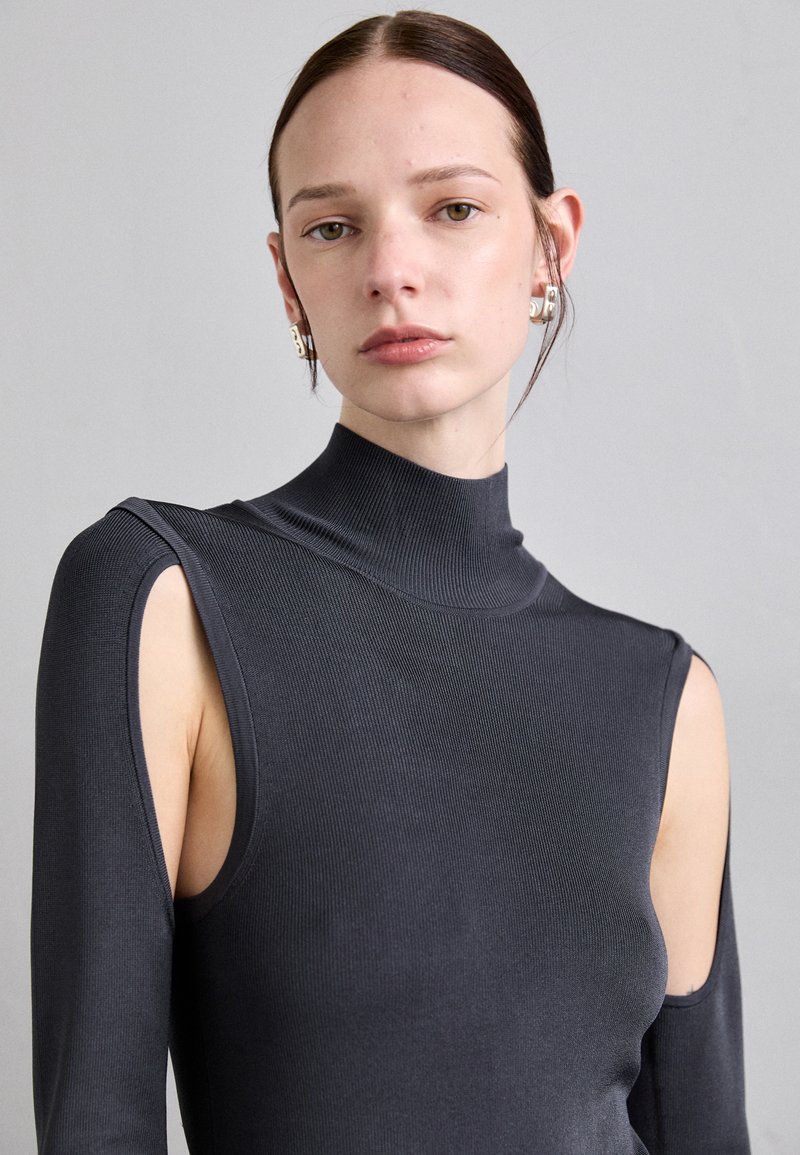 Slank fitting, hooghals top in donkergrijze ribstof. Heeft open schouderuitsnijdingen en een textuur op het oppervlak. Minimalistisch ontwerp.