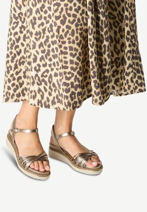 Kilklackssandaletter med metalliska bruna remmar, med en flätad design och ankelspenne, i kombination med en leopardmönstrad kjol.