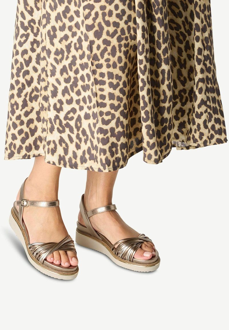 Kilklackssandaletter med metalliska bruna remmar, med en flätad design och ankelspenne, i kombination med en leopardmönstrad kjol.