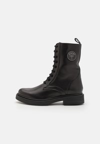Bottine en cuir noir à lacets, bout arrondi et talon épais. Dispose d'un patch logo sur le côté et de lacets texturés.
