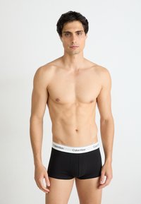 Zwarte katoenen boxershorts met een witte tailleband waarop 'Calvin Klein' in zwarte letters staat. De pasvorm is strak en de stof lijkt glad te zijn.