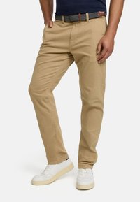 Beige cotton pants with a straight fit, featuring a flat front design. Paired with a patterned belt and white sneakers.