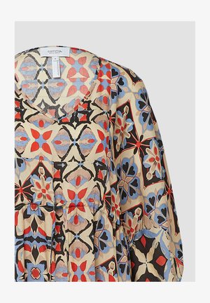 Musterbluse mit V-Ausschnitt, die eine Mischung aus roten, blauen und schwarzen Blumenmustern auf einem beigen Hintergrund zeigt und aus leichtem Stoff besteht.