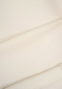 Tkanina w kolorze kremowym, o miękkiej, prążkowanej fakturze. Materiał wydaje się elastyczny i gładki, z jednolitą, spójną powierzchnią.